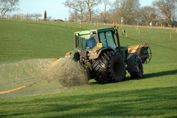 Hose behind a tractor spraying slurry in a field.