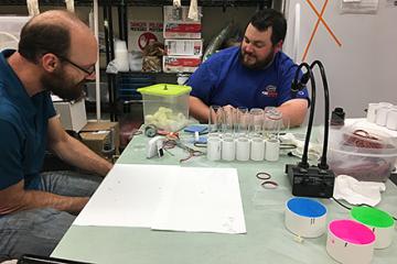 Two researchers sit at a table examining equipment