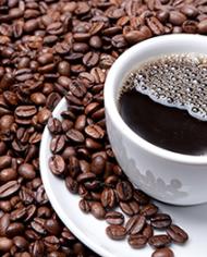 Coffee in a white cup sitting on a white saucer surrounded by coffee beans