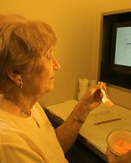 A woman sitting in front of a monitor eating cantaloupe